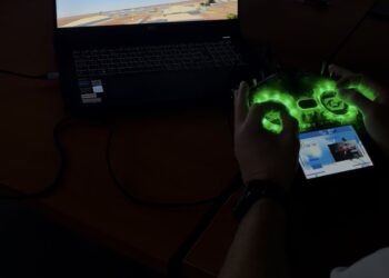 An operator using a radio controller with an FPV flight simulator on a laptop