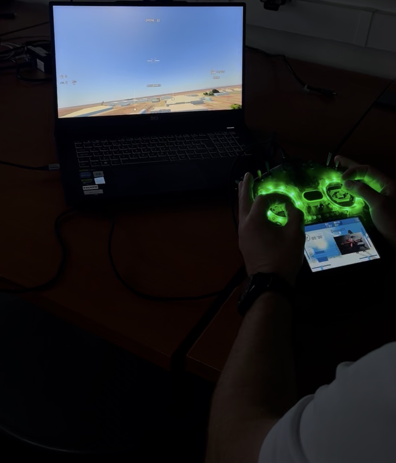 An operator using a radio controller with an FPV flight simulator on a laptop